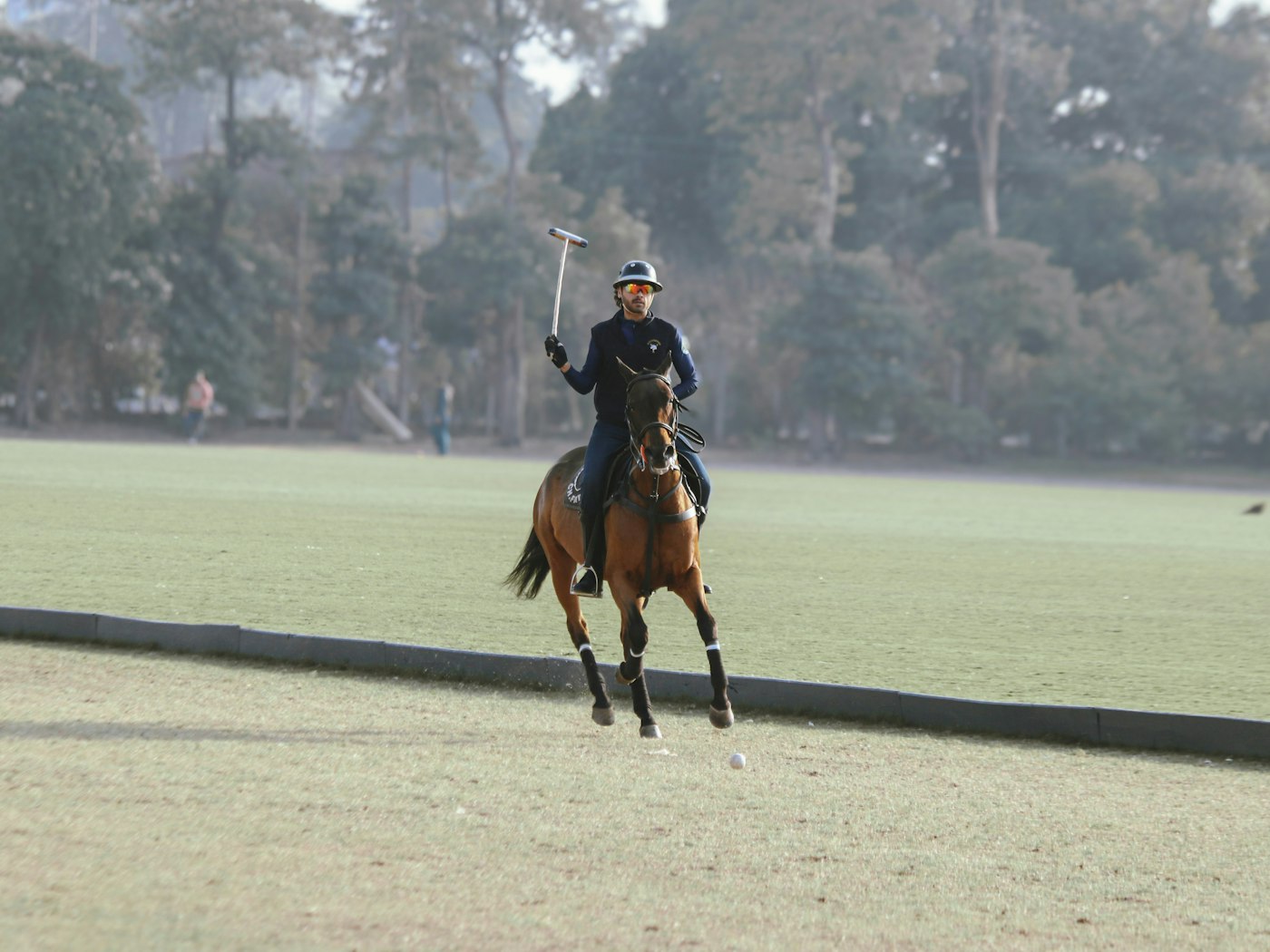 A polo player galloping across a wide green field